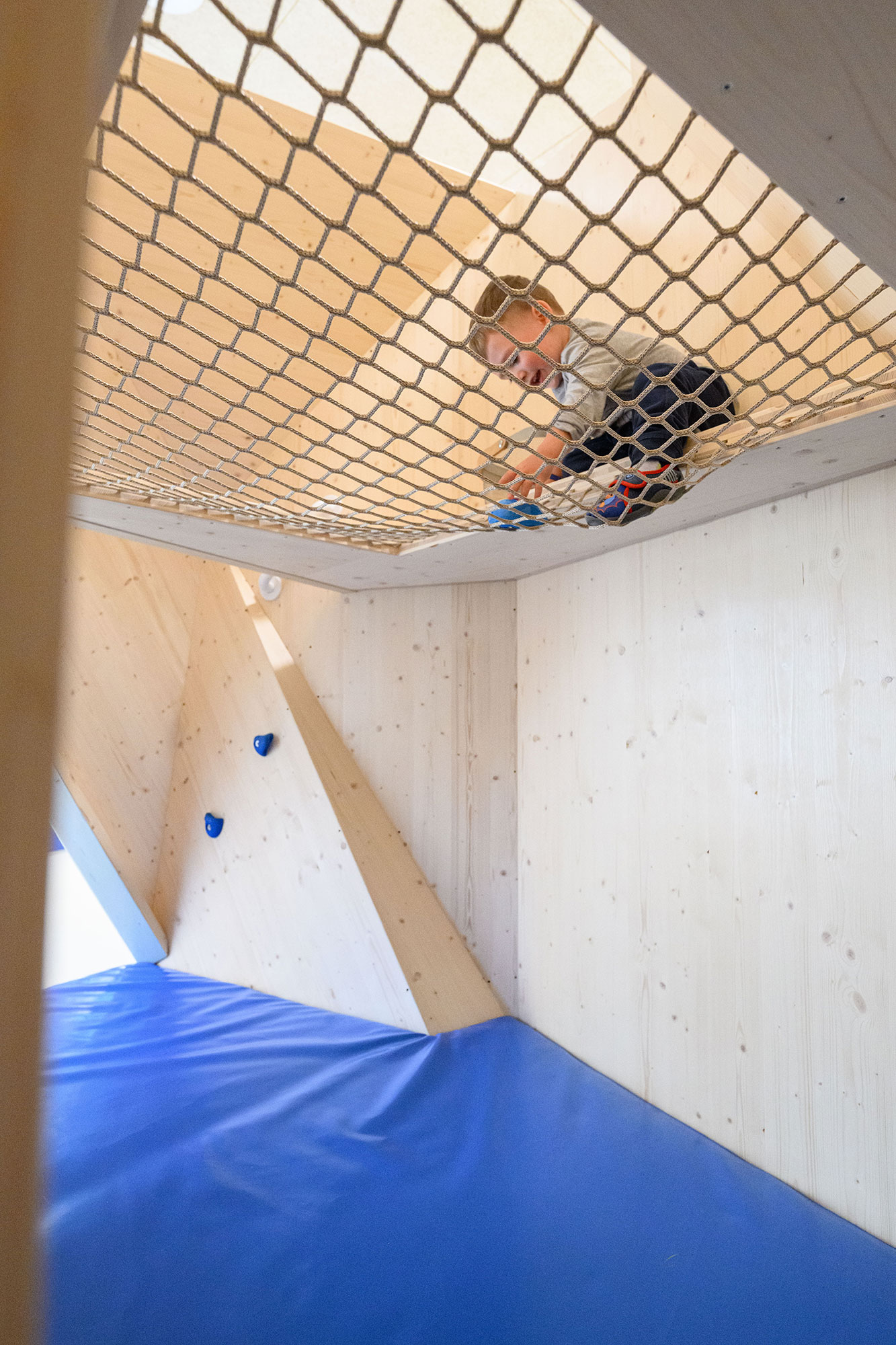 Ein Kind im Kletternetz in einer Kletterlandschaft in einer Kita oder Kindergarten. Individuelle gebaute Möbel für Kindergärten und Kitas